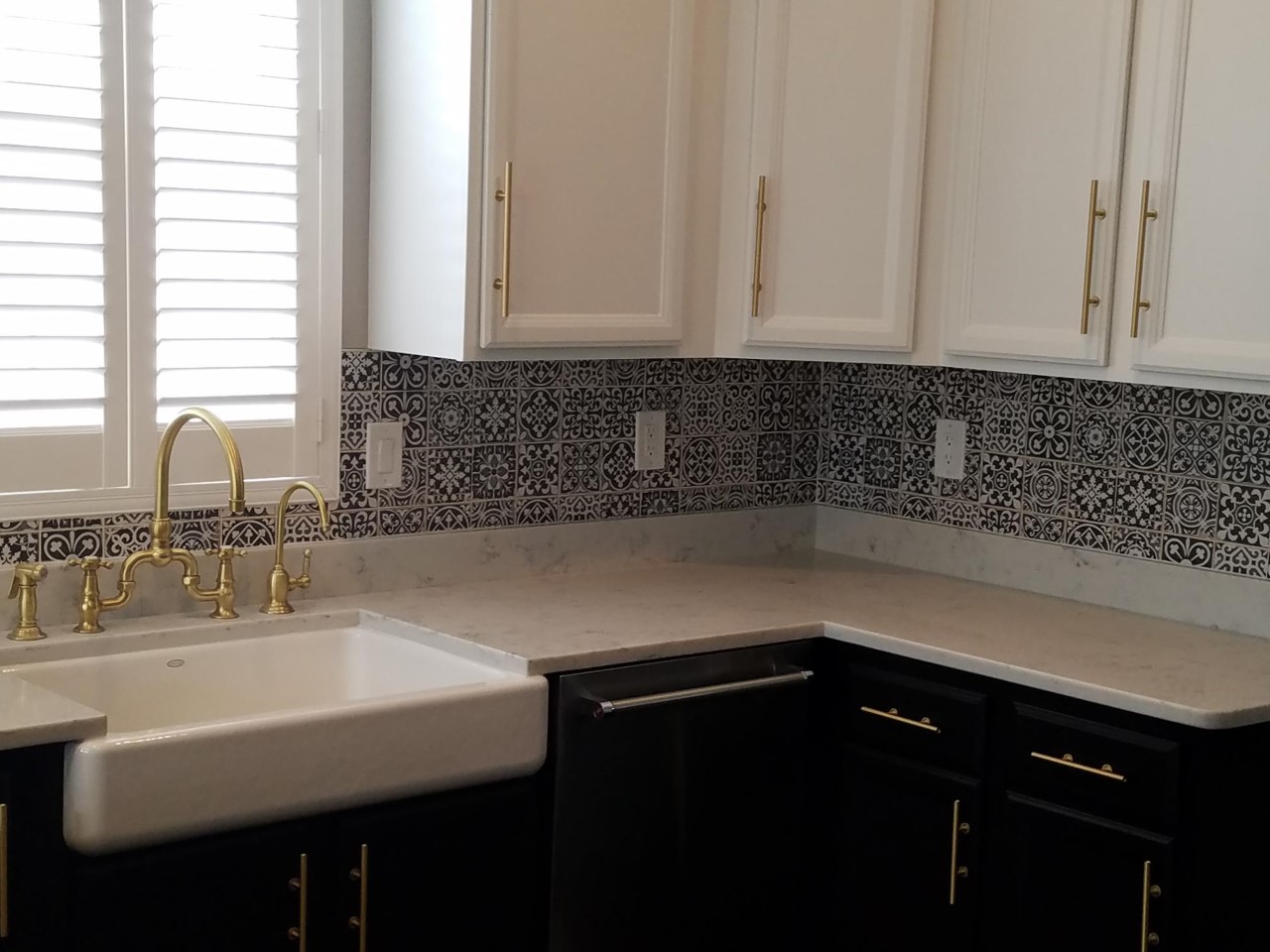 newly modeled kitchen with white upper cabinets, dark lower cabinets, new gold hardware, beautiful granite countertops and a mosaic tile backsplash. Notice the farmhouse sink centered on the white shuttered window overlooking the backyard.