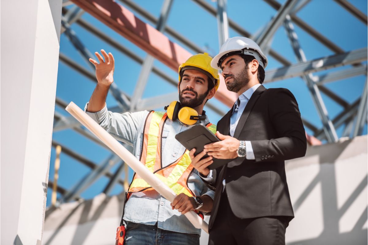 two men wearing hard hats standing in a construction site discussing the project. There are benefits to working with a Professional Remodeling Contractor