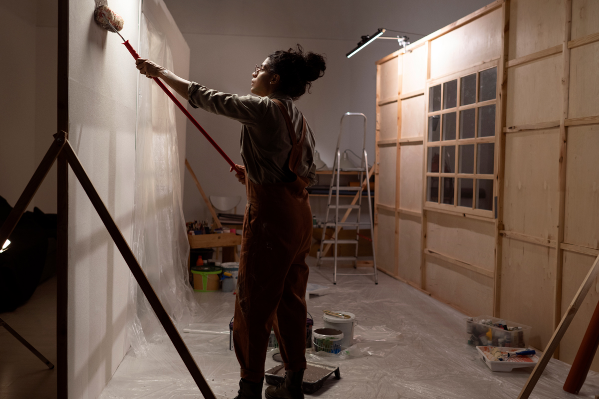 female working on a basement remodel, painting new hung drywall.