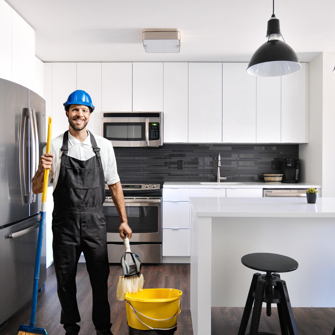 Remodeling specialist with a blue hard hat, holding a mop and broom in a new renovated kitchen. At White Oak our job isn't complete until your space is neat and tidy. We always leave a job site better than we found it.