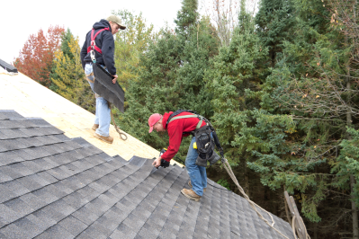 photo of two roofers on top of a home replacing the roof damaged in a recent storm